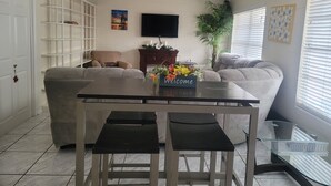 Un salon comprenant une table à manger, deux canapés, un téléviseur et une bibliothèque.