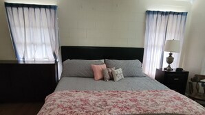 Un lit bien fait, avec une couvre-lit à motifs floraux, une tête de lit sombre et plusieurs oreillers.