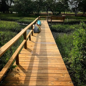 Un paseo marítimo de madera que atraviesa un área cubierta de césped con árboles al fondo.