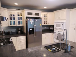 A modern kitchen with white cabinets, a stainless steel refrigerator, a microwave, and a sink with a dish rack.