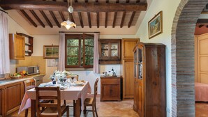 A rustic kitchen with wooden cabinets, a dining table set for four, and a large window with curtains. - Villa Riparbella (Riparbella)