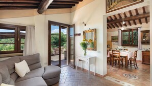 A spacious living area with a sofa, a dining table set for four, and a view of the outdoors through large windows. - Villa Riparbella (Riparbella)