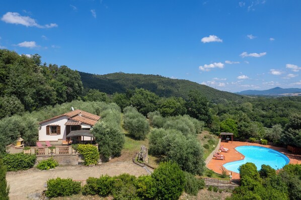 Une villa avec piscine, entourée d’une végétation luxuriante et de collines.