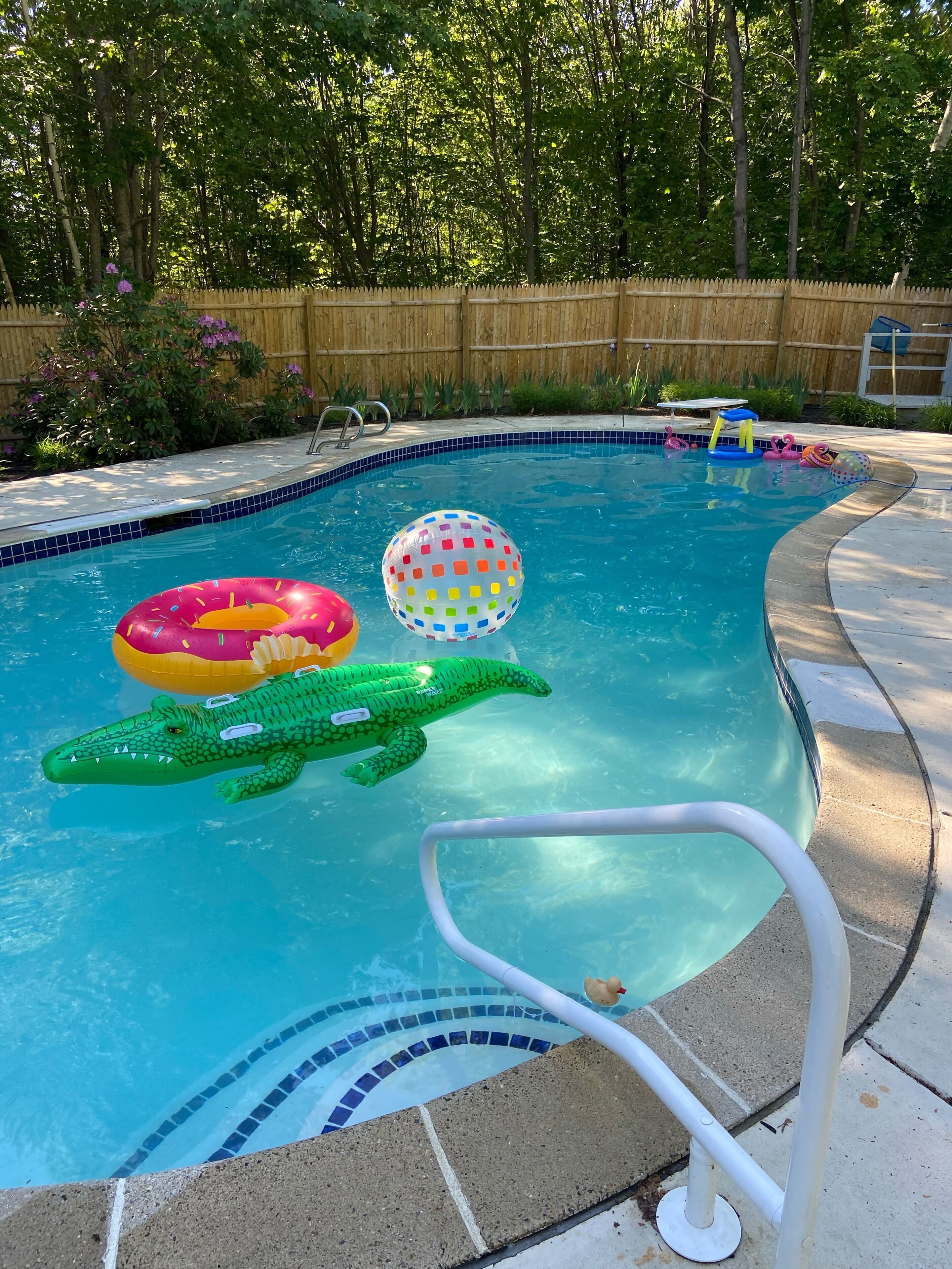 Una piscina con valla de madera, escalera de piscina y juguetes inflables.
