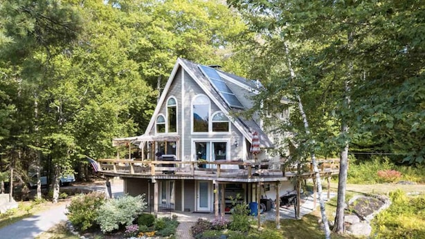 Een twee verdiepingen tellend huis met een ruim terras, omringd door weelderige begroeiing.