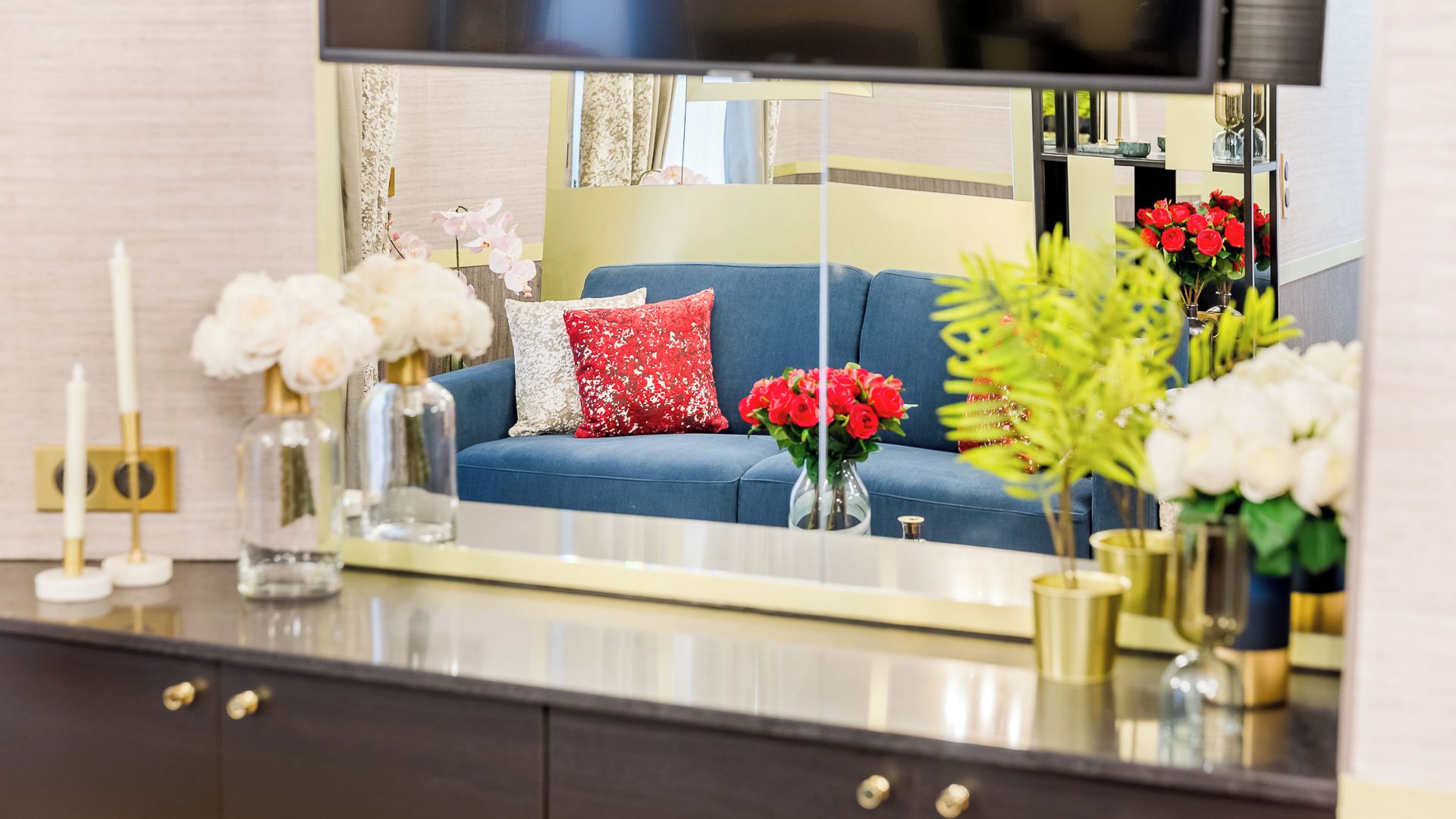 A modern living room with a blue sofa, a red pillow, and various decorative items including vases with flowers.