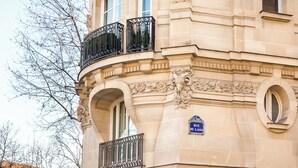 Un bâtiment doté d’éléments architecturaux décoratifs, notamment un balcon orné de balustrades en fer forgé et une enseigne indiquant « RUE DU LAOS ».