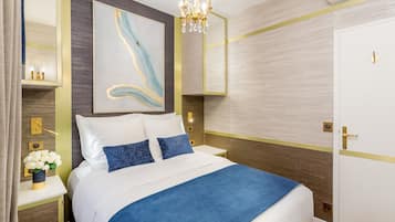 A neatly arranged hotel room with a large bed, a bedside table with a vase of flowers, a wall-mounted artwork, and a modern chandelier.