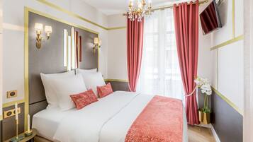 Een hotelkamer met een groot bed, een kroonluchter, een flatscreen-tv en rode gordijnen.