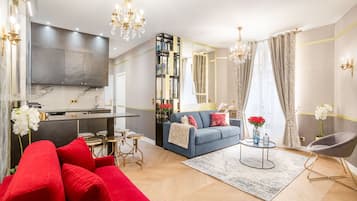 Een moderne woonkamer met een blauwe bank, rode kussens, een salontafel en een kroonluchter.