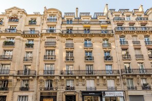 A multi-story building with ornate architectural details, including balconies with wrought iron railings and decorative moldings. - Merveil - Luxury Suite - Tour Eiffel - Laos (Paris)