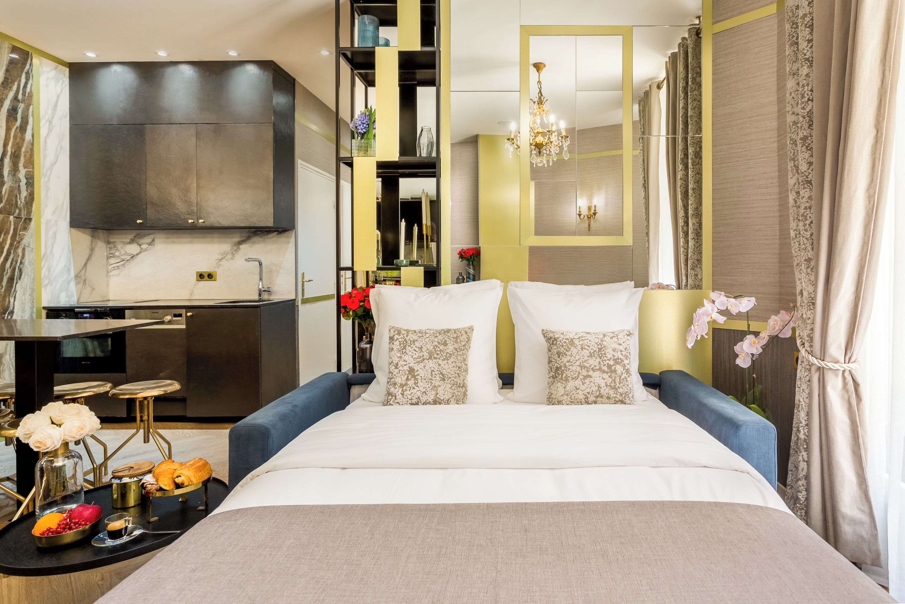 Camera d'albergo moderna con un letto grande, un angolo cottura e un bagno visibile tramite una parete divisoria in vetro.