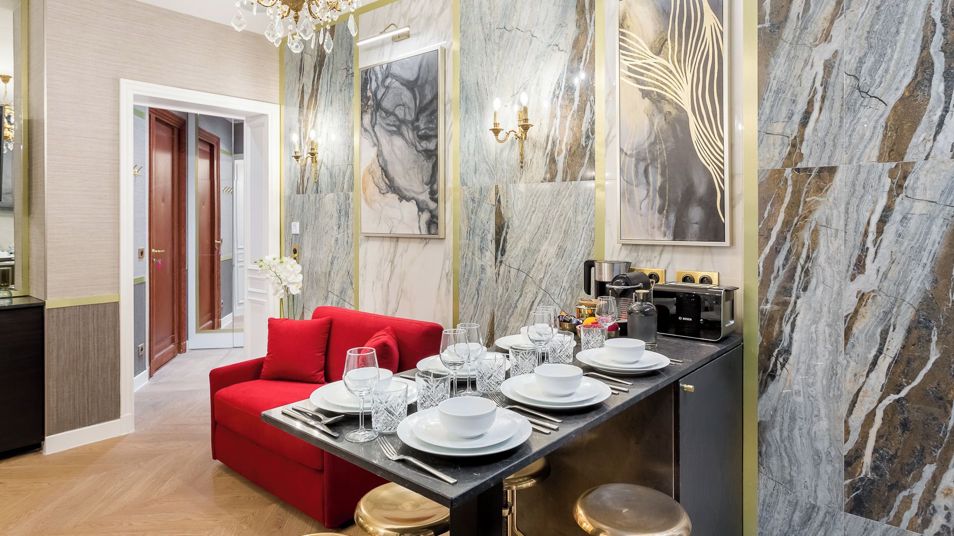 A modern dining area with a red sofa, a marble wall, and a kitchen counter with a Bosch coffee machine.