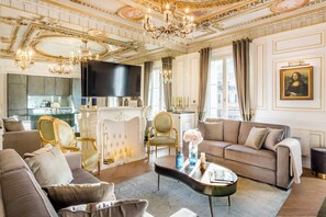 A luxurious living room with a fireplace, elegant furniture, and a chandelier. - Merveil - Signature Suite - Louvre - Marcel I (Paris)