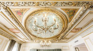 An ornate ceiling with a central chandelier, detailed moldings, and floral motifs. - Merveil - Signature Suite - Louvre - Marcel I (Paris)