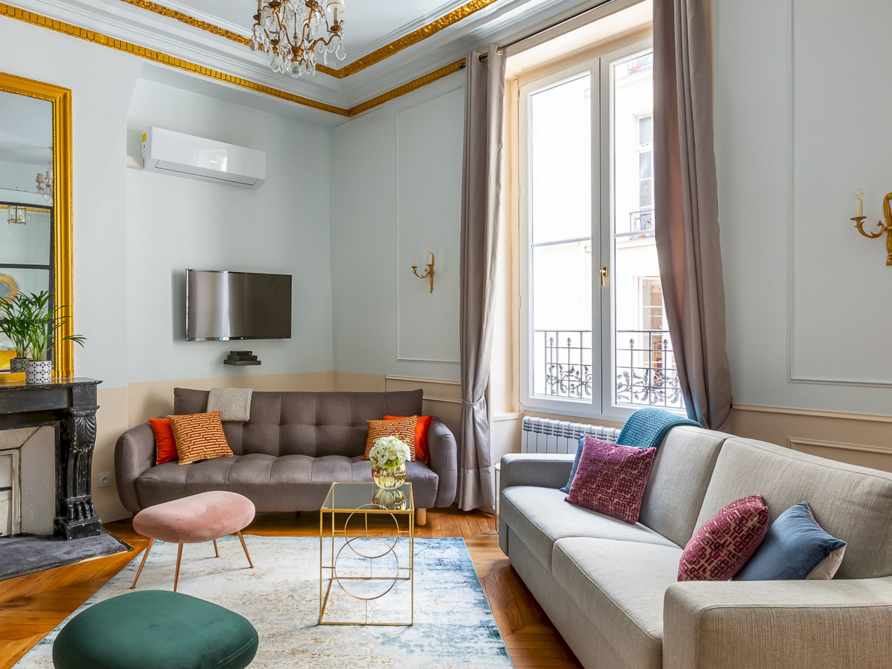 A modern living room with a grey sofa, a green ottoman, and a TV mounted on the wall.