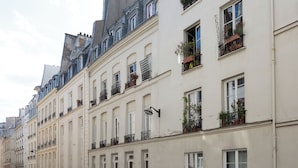 A row of classic European-style buildings with uniform facades, multiple windows, and balconies with potted plants.