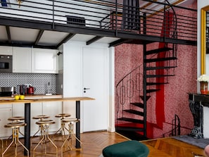 Cocina moderna con armarios blancos, encimera de madera y una escalera en espiral negra frente a una pared con diseño rojo.