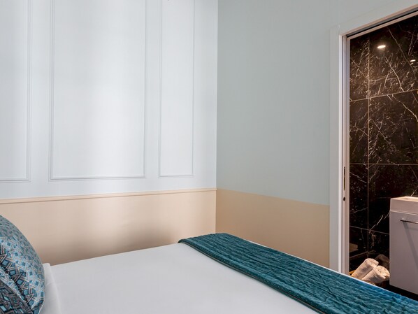 A hotel room with a bed, a door with a marble pattern, and a towel rack with towels. - Merveil - Luxury Suite - Louvre - Aboukir I (Paris)