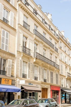 A multi-story building with balconies, storefronts, and parked cars.