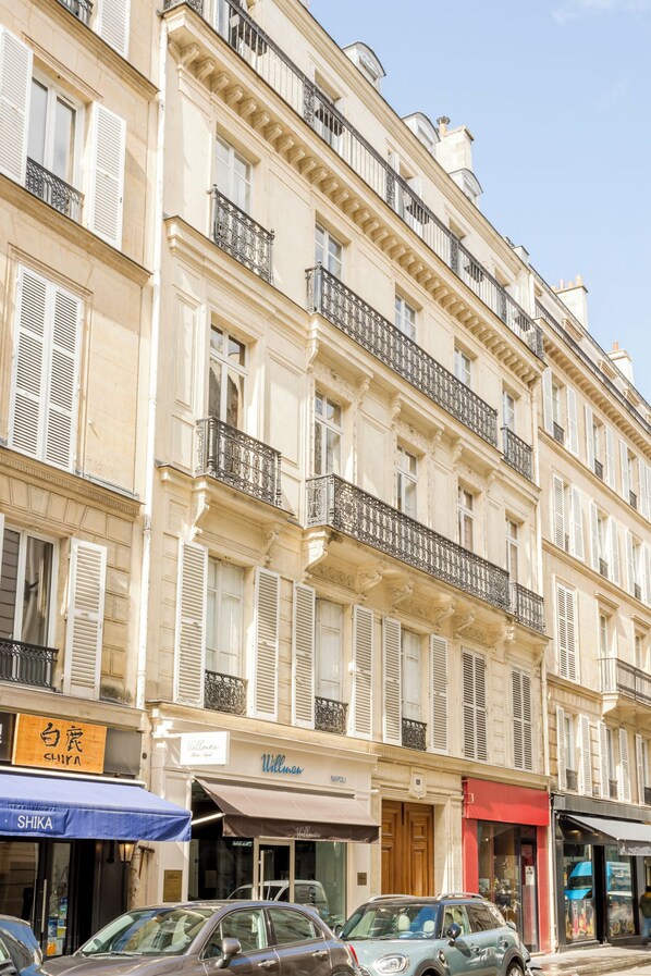 A multi-story building with balconies, storefronts, and parked cars.
