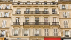 A multi-story building with a classic architectural style, featuring balconies with wrought iron railings and shutters.