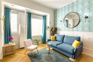 Een woonkamer met een blauwe bank, turquoise gordijnen, een ronde spiegel en een tapijtend met een patroon.