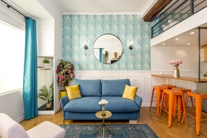 A living room with a blue sofa, yellow cushions, a round mirror, and orange bar stools. - Luxury Suite - Champs Elysées - Mermoz (Paris)