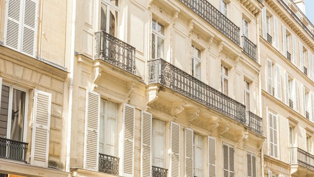 A multi-story building with balconies, storefronts, and parked cars.
