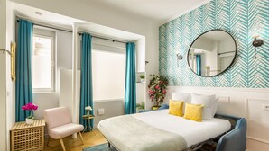 A bedroom with a bed, a chair, a small table, and a window with curtains.
