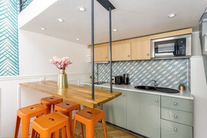 A modern kitchen with a wooden table and orange stools, a microwave, and a tiled backsplash. - Luxury Suite - Champs Elysées - Mermoz (Paris)