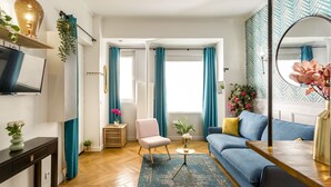 A modern living room with a blue sofa, a pink chair, a TV on a stand, and a large mirror.