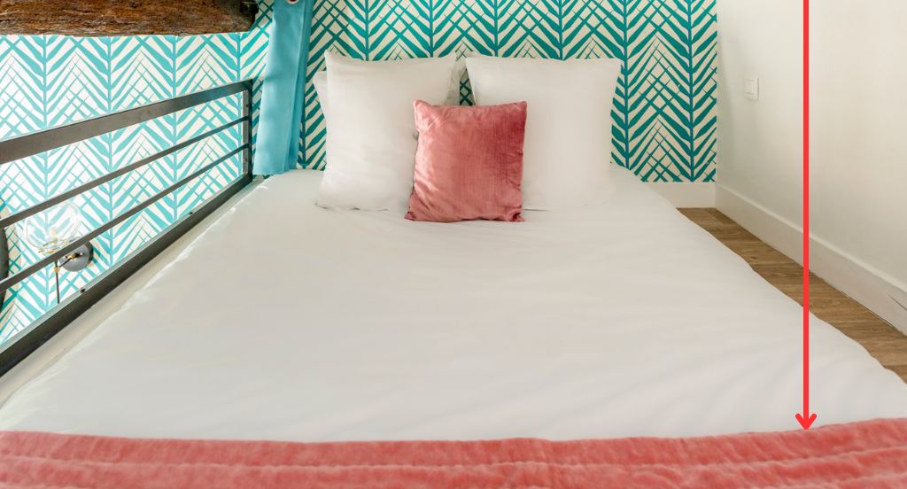 A bed with a white mattress and two pillows, one pink and one white, against a wall with a geometric pattern.