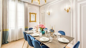 A dining room with a long table set for six, blue chairs, white plates, and a vase of pink flowers. - Merveil - Signature Suite - Louvre - Victoria (Paris)