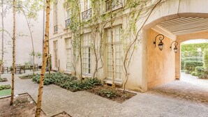 A courtyard with a pergola, stone flooring, and a building with large windows and a wall-mounted lantern. - Merveil - Luxury Suite - Marais - Archives I (Paris)
