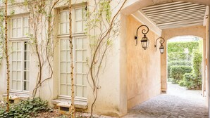 A covered walkway with a stone floor, a bench, and a wall with climbing plants. - Merveil - Luxury Suite - Marais - Archives I (Paris)