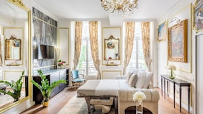 A luxurious bedroom with a large bed, a television, a sofa, and a dining table. - Merveil - Luxury Serviced Apartment - Aboukir VI (Paris)