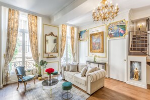 A well-lit living room with a sofa, armchairs, a chandelier, and artwork on the walls.