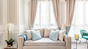 A well-lit room with a beige sofa, a small table with a candle, and a potted plant. - Merveil - Luxury Suite - Louvre - Marcel II (Paris)