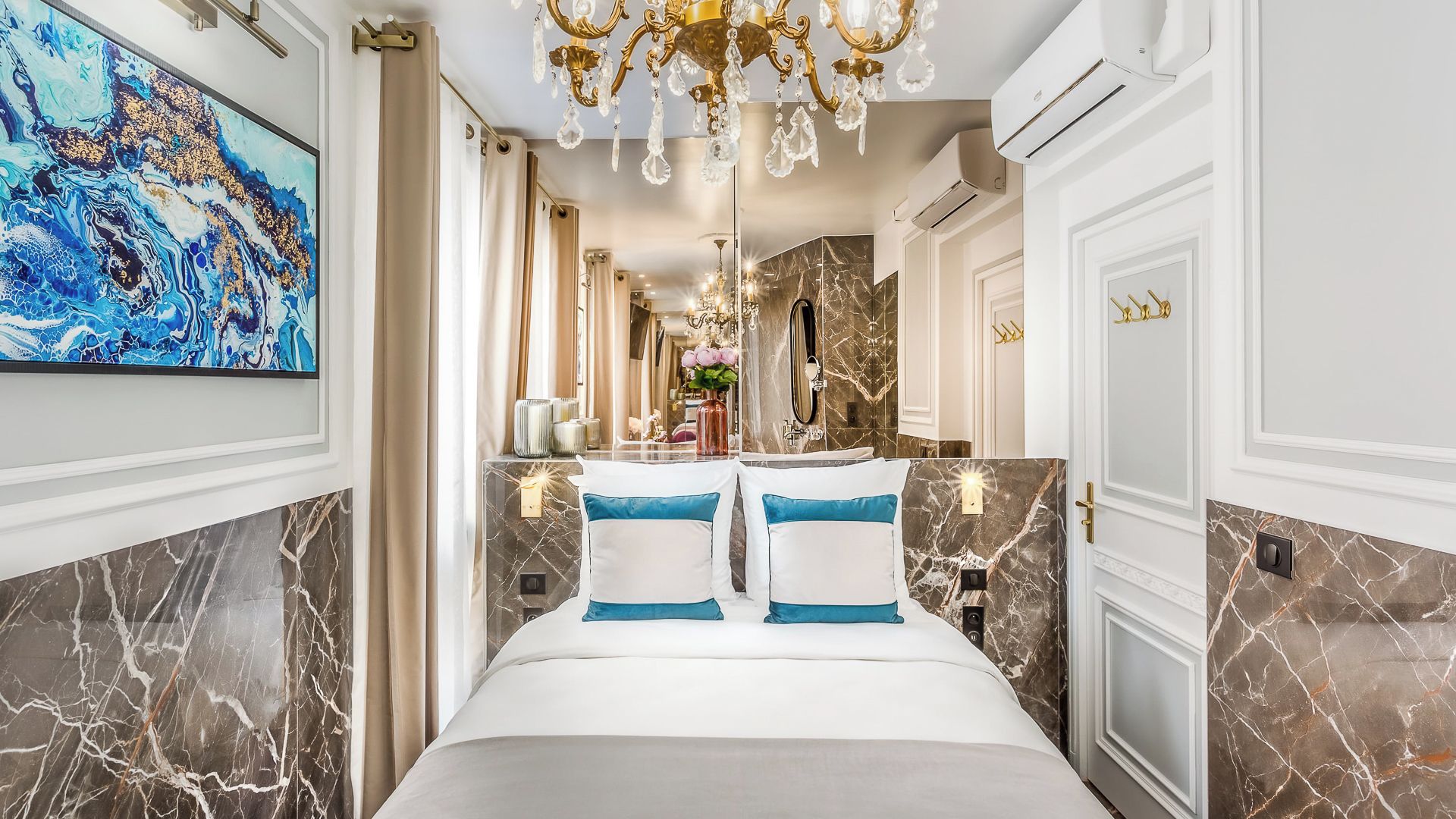 A luxurious hotel room with a marble bathroom, a large bed with blue pillows, and a chandelier.