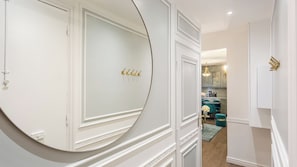 A hallway with white walls and a round mirror with gold hooks. - Merveil - Luxury Suite - Louvre - Marcel II (Paris)