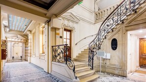 A grand staircase with ornate iron railings, leading to a landing with a door. - Merveil - Luxury Suite - Louvre - Marcel II (Paris)