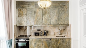 A kitchen with a marble countertop, a built-in oven, a dishwasher, and wooden cabinets above. - Merveil - Luxury Suite - Louvre - Marcel II (Paris)