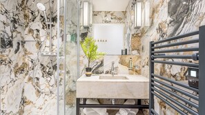 Un baño con salpicadero de mármol, un lavabo con espejo, ducha y toallero.