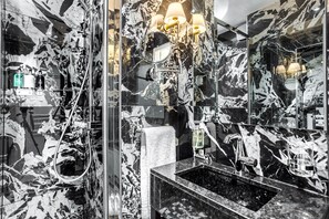 Un baño con pared de mármol, un lavabo con espejo y zona de ducha.