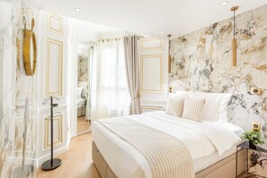 A modern bedroom with a large bed, a marble wall, and a gold-framed mirror.