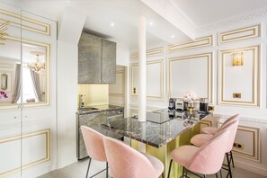 A modern kitchen with marble countertops, gold accents, and pink bar stools.