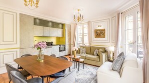 A modern living room with a dining table, sofa, and kitchen in the background.