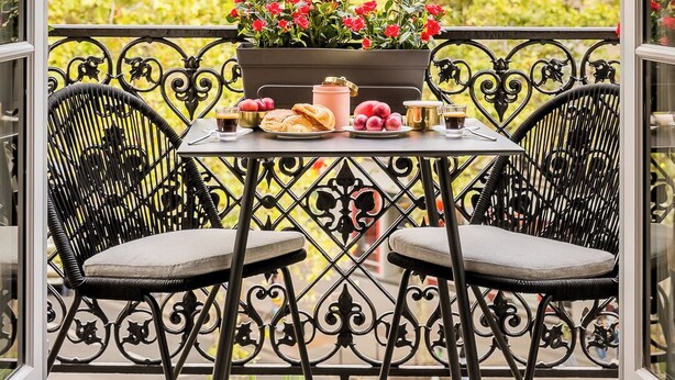 Un balcon avec une table dressée pour deux personnes, agrémenté d’un vase de fleurs, d’une théière et d’une tasse.