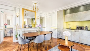A dining room with a wooden table, grey upholstered chairs, a chandelier, and a large mirror.